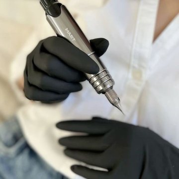 Майстер у рукавичках тримає тату-машинку