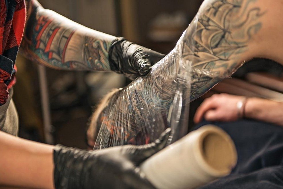 Мастер обматывает татуированную руку пленкой